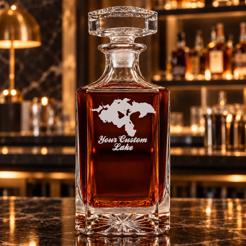 Minimalist square decanter alone with frosted generic lake artwork, amber whiskey, and a warm bar background.