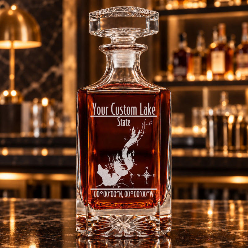 Modern square decanter alone with frosted generic lake artwork, amber whiskey, and a warm bar background.