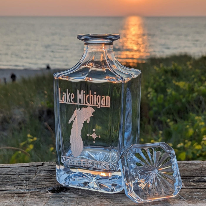 Lifestyle photo: Lake Michigan engraved whiskey decanter and stopper on a wooden rail at sunset by the water
