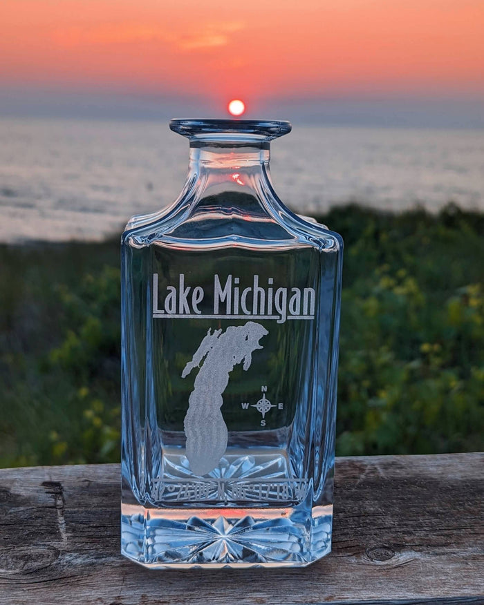 Lifestyle photo: Lake Michigan engraved whiskey decanter on a wooden rail at sunset over the water